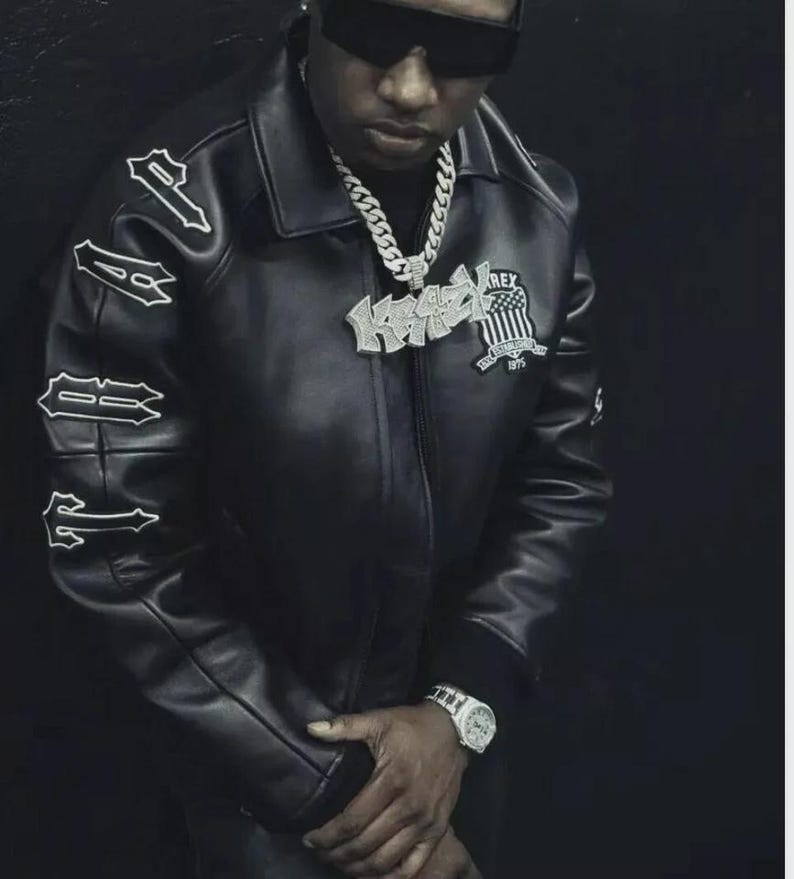 May include: Black leather jacket with white lettering on the sleeves and a patch on the chest. The jacket has a collar and a zipper closure. A silver chain necklace and a wristwatch are also visible.