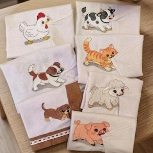 May include: A collection of six white fabric cloths, each featuring a different embroidered animal: a white chicken, a black and white cow, an orange tabby cat, a brown and white puppy, a fluffy white sheep, and a pink piglet.
