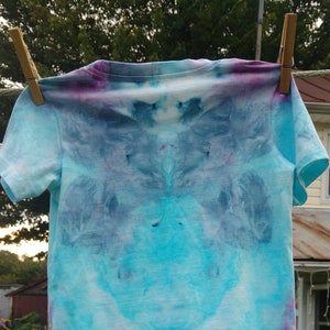 May include: A light blue tie-dye t-shirt with a white background and purple and blue accents.