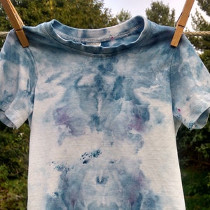 May include: A blue and white tie-dye t-shirt with a light blue and white pattern. The shirt has short sleeves and a crew neck.
