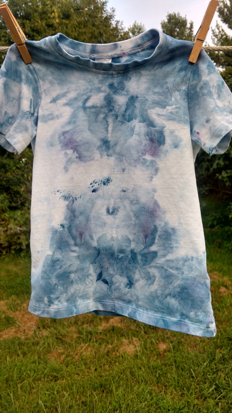 May include: A blue and white tie-dye t-shirt with a light blue and white pattern. The shirt has short sleeves and a crew neck.