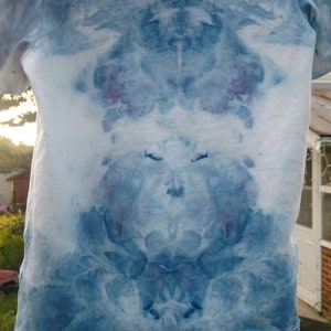 May include: A blue tie-dye t-shirt with a symmetrical pattern. The shirt is hanging on a clothesline.