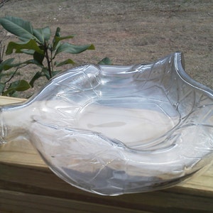 Könnte beinhalten: Eine klare Glasflasche mit goldenem Deckel wurde zu einer dekorativen Schale umfunktioniert. Die Flasche wurde geschnitten und zu einer Schale mit welligem Rand geformt. Das Glas hat ein strukturiertes Muster.