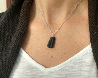 May include: A silver chain necklace with a black, faceted, rectangular pendant.
