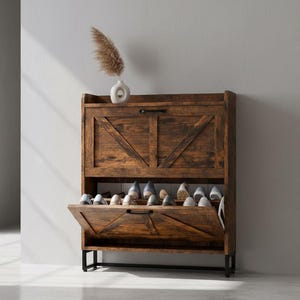 May include: A rustic wooden shoe cabinet with two compartments, one open and one closed, displaying various shoes. The cabinet has a dark brown finish and black metal legs. A small white vase with a decorative plant sits on top.