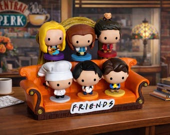 May include: A decorative orange couch with six Friends character figurines. The figurines have large heads and small bodies. The couch has the word "FRIENDS" on the front. The background includes a coffee shop scene.