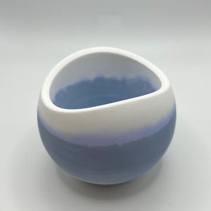 Könnte beinhalten: Eine kleine, runde Keramikschale mit einem einzigartigen Design. Die Schale ist mit einem Farbverlauf bemalt, der von Weiß oben nach Hellblau am Boden übergeht. Der Innenraum ist ebenfalls hellblau.