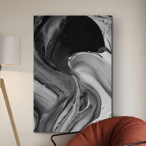 May include: Abstract black and white artwork with flowing, textured brushstrokes. The painting hangs on a wall above a rust-colored beanbag chair with black metal frame. A wooden tripod floor lamp and a black side table are in the foreground.