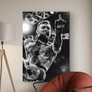 Puede incluir: Una impresión de arte mural en blanco y negro que muestra a un atleta sin camisa con tatuajes y guantes de UFC, levantando el dedo medio. El atleta está capturado en una pose dinámica con un brazo extendido, mostrando musculatura y equipo deportivo.