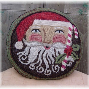 May include: A round, brown, green, and red wool rug with a Santa Claus face in the center. The Santa has a white beard, a red hat with a white trim, and a candy cane in his hand.