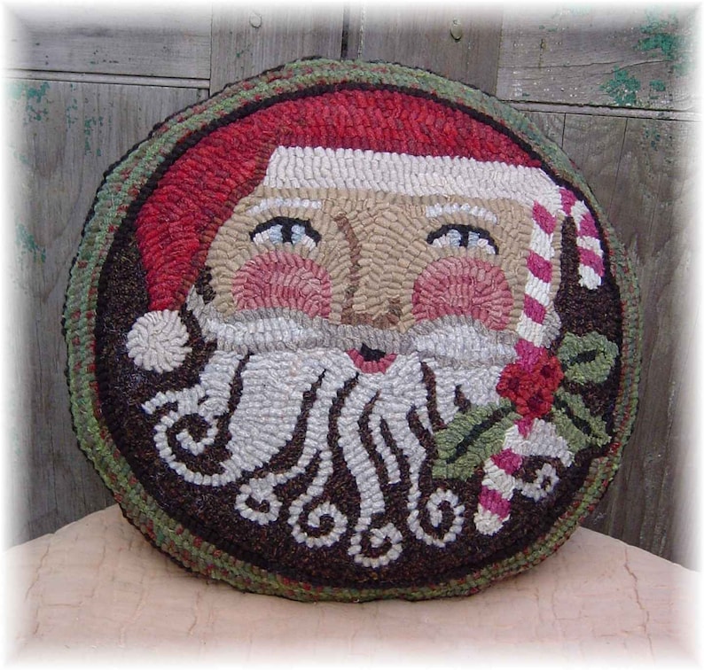 May include: A round, brown, green, and red wool rug with a Santa Claus face in the center. The Santa has a white beard, a red hat with a white trim, and a candy cane in his hand.