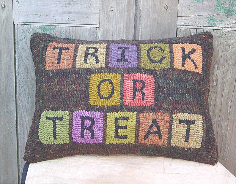 Peut inclure: Un coussin brun avec les mots "Trick or Treat" &eacute;crits en carr&eacute;s color&eacute;s. Chaque lettre est dans un carr&eacute; de couleur diff&eacute;rente, avec les "T" en vert, les "R" en violet, le "I" en orange, le "C" en jaune, le "O" en rose et le "E" en marron.