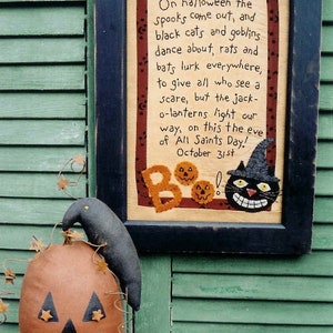 May include: A framed Halloween-themed needlepoint with a black cat and the text "On halloween the spooks come out, and black cats and goblins dance about, rats and bats lurk everywhere, to give all who see a scare, but the jack-o-lanterns light our way, on this the eve of All Saints Day! October 31st". A brown pumpkin with a black jack-o-lantern face and a black crow sits in front of the frame.