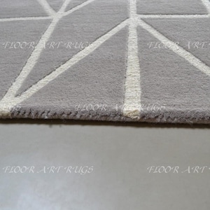 May include: A gray area rug featuring a white geometric pattern of intersecting lines. The rug has a textured pile surface and includes the repeating text FLOOR ART RUGS printed across the fabric in a light font.
