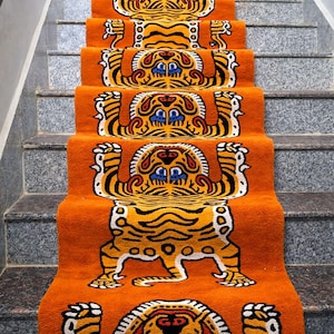 May include: Orange stair runners with a repeating tiger design. Each runner features a full tiger image with black stripes, white accents, and blue and red details. The stairs are made of gray stone.