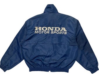 May include: A navy blue Honda Motor Sports jacket with a stand-up collar and a zipper closure. The white text "HONDA MOTOR SPORTS" is embroidered on the back. The jacket has elastic cuffs and a bottom hem.