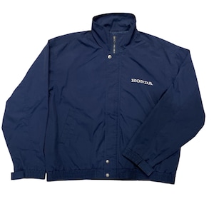 May include: Navy blue jacket with a stand-up collar and a zipper closure. The jacket features the word "HONDA" in white lettering on the chest. It has two front pockets and elastic cuffs and hem.