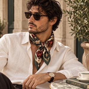 Peut inclure: Une chemise en lin blanc à manches longues associée à un foulard en soie vert foncé orné d'un imprimé botanique de grenades, de fleurs blanches et d'une étoile boussole dorée. Le foulard est noué autour du cou, complétant la chemise claire.