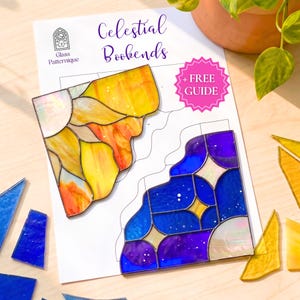 Op de afbeelding: Een paar gebrandschilderde hemelse boekensteunen in gele, oranje en blauwe tinten, met een patroonhandleiding. De boekensteunen zijn ontworpen met een zon- en sterrennachtthema. De woorden "Celestial Bookends" en "+ FREE GUIDE" zijn zichtbaar.