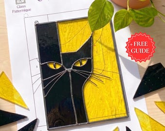 Puede incluir: Un panel de gato de vidriera con un diseño negro y amarillo. La cara del gato es negra, con ojos y bigotes amarillos, sobre un fondo amarillo. El panel está sobre un papel blanco con las palabras "Cat Panel" y "Glass Patternique".