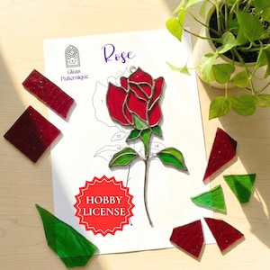Peut inclure: Un kit de bricolage de rose en vitrail avec des morceaux de verre rouges et verts. Le kit comprend un patron avec le mot "Rose" et le texte "Glass Patternique". Un autocollant rouge indique "Hobby License".