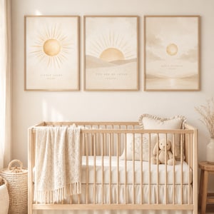 May include: Three framed art prints with sun illustrations and text, above a wooden crib with a cream-colored blanket and bedding. The prints feature the phrases "Little Light", "You Are So Loved", and "Hello Sunshine". A teddy bear sits on the crib.
