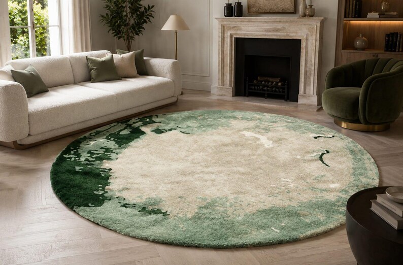 May include: A large round area rug featuring an abstract pattern with a central cream-colored field surrounded by blended gradients of sage green and deep forest green, creating a textured, layered appearance across the circular surface.