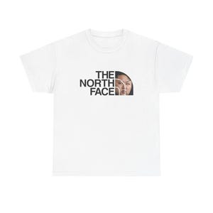 Può includere: T-shirt bianca con la scritta "THE NORTH FACE" in nero, con il volto di una donna incorporato nel logo. La maglietta è un classico girocollo.