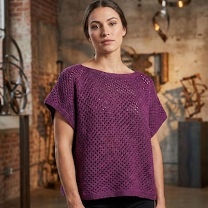Può includere: Un top in maglia color prugna a maniche corte con scollo a barchetta. Il design a trama aperta crea un aspetto strutturato. Il top è indossato da una persona davanti a un muro di mattoni.