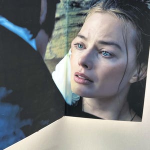 May include: A close-up of a woman with fair skin and blue eyes. The woman is looking off to the side with a concerned expression. The image is from a book or magazine, with a white border and a dark background.