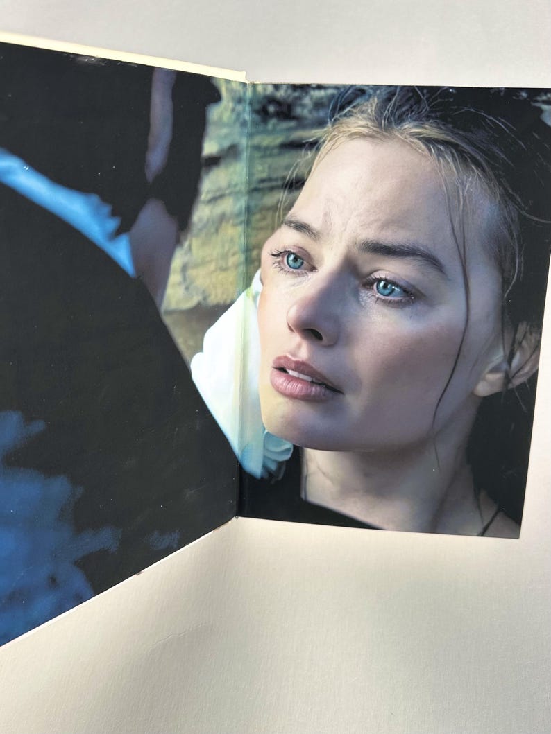 May include: A close-up of a woman with fair skin and blue eyes. The woman is looking off to the side with a concerned expression. The image is from a book or magazine, with a white border and a dark background.