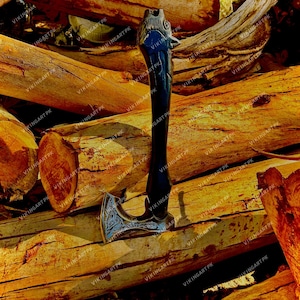 May include: A handcrafted axe with a dark handle and a silver blade. The handle features a carved wolf head design. The axe is resting on a pile of wooden logs, showcasing its rustic aesthetic. The blade has intricate engraved patterns.