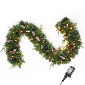 May include: A festive artificial evergreen garland featuring lush green pine needles, scattered brown pinecones, and warm white LED string lights. The garland is arranged in an S-shape and includes a black electrical power adapter with a plug.