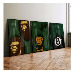 Peut inclure: Trois impressions d'art encadrées contre un mur. Les impressions présentent une tête de singe marron et dorée, un personnage de singe vert et une boule huit noire et blanche, le tout sur fond vert. Les cadres sont noirs.