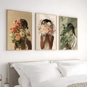 May include: Three framed art prints featuring illustrations of figures holding bouquets of flowers. The artwork has a neutral color palette with beige, peach, and green tones. The figures' faces are obscured by the flowers, creating a sense of mystery.