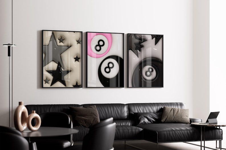 May include: Three framed art prints with black frames. The prints feature abstract designs: stars, a pink and black eight ball, and a black eight ball. The artwork hangs above a black leather sectional sofa.