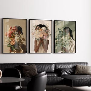May include: Three framed art prints featuring figures with floral arrangements obscuring their faces. The prints have black frames and are hung above a black leather sectional sofa. The color palette includes beige, pink, and green.