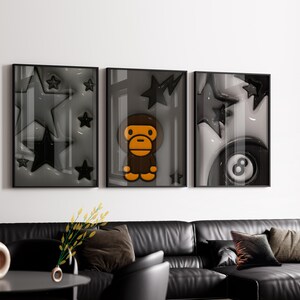 Puede incluir: Un conjunto de tres l&aacute;minas de arte mural enmarcadas con una paleta de colores monocrom&aacute;ticos en gris y negro. La l&aacute;mina izquierda muestra varias estrellas, la central muestra un personaje de mono y la derecha una bola ocho negra.
