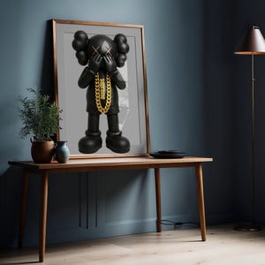 Puede incluir: Una impresi&oacute;n de arte de pared enmarcada que presenta una figura negra de KAWS con ojos en forma de X, manos cubriendo su rostro y un collar de cadena de color dorado con la palabra supreme impresa en min&uacute;sculas alrededor del cuello.