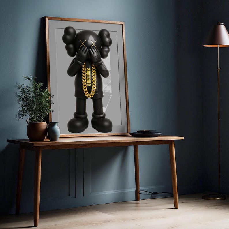 Puede incluir: Una impresi&oacute;n de arte de pared enmarcada que presenta una figura negra de KAWS con ojos en forma de X, manos cubriendo su rostro y un collar de cadena de color dorado con la palabra supreme impresa en min&uacute;sculas alrededor del cuello.