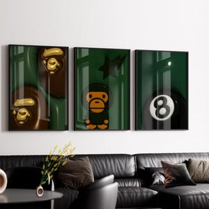 Puede incluir: Un conjunto de tres l&aacute;minas de arte enmarcadas con fondo verde oscuro. La primera l&aacute;mina muestra dos caras de mono marrones, la segunda presenta un personaje de mono con una estrella y la tercera representa una bola de billar n&uacute;mero ocho.