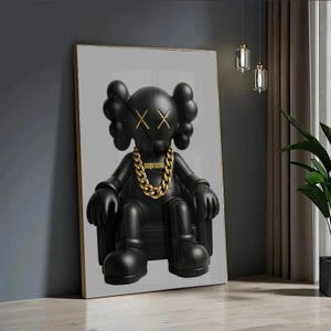 Puede incluir: Una impresi&oacute;n de arte mural enmarcada que presenta un personaje de dibujos animados negro mate con ojos en forma de X sentado en una silla. El personaje lleva una cadena dorada gruesa con la palabra Supreme impresa en letras doradas en el pecho.