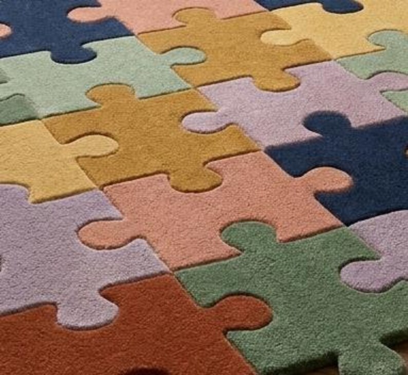 May include: A colorful puzzle-piece rug in shades of blue, green, yellow, orange, and purple. The rug's design features large, interlocking puzzle pieces, creating a playful and inviting floor covering. The rug is made of a soft material.