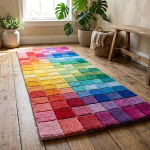 Puede incluir: Una alfombra rectangular con un vibrante diseño de gradiente de arcoíris. La alfombra presenta un patrón de cuadrados en tonos de rojo, naranja, amarillo, verde, azul y morado. La alfombra está colocada sobre un suelo de madera.