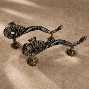 May include: A pair of bronze-effect snake-shaped door handles. Each handle has a detailed snake head and body with a scale pattern. They are mounted on circular bases, offering a decorative and functional hardware set for doors.