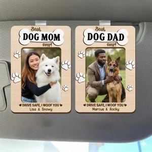 Puede incluir: Dos adornos de visera de coche de madera. Uno dice "¡La mejor mamá perruna de la historia!" con una foto de una mujer y un perro blanco. El otro dice "¡El mejor papá perruno de la historia!" con una foto de un hombre y un pastor alemán.