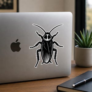 Op de afbeelding: Een zwart-witte sticker van een kakkerlak met gedetailleerde lijnen, lange antennes en stekelige poten, aangebracht in het midden van de deksel van een zilveren laptop. De insectillustratie is gestileerd met hoog contrast en een witte rand.