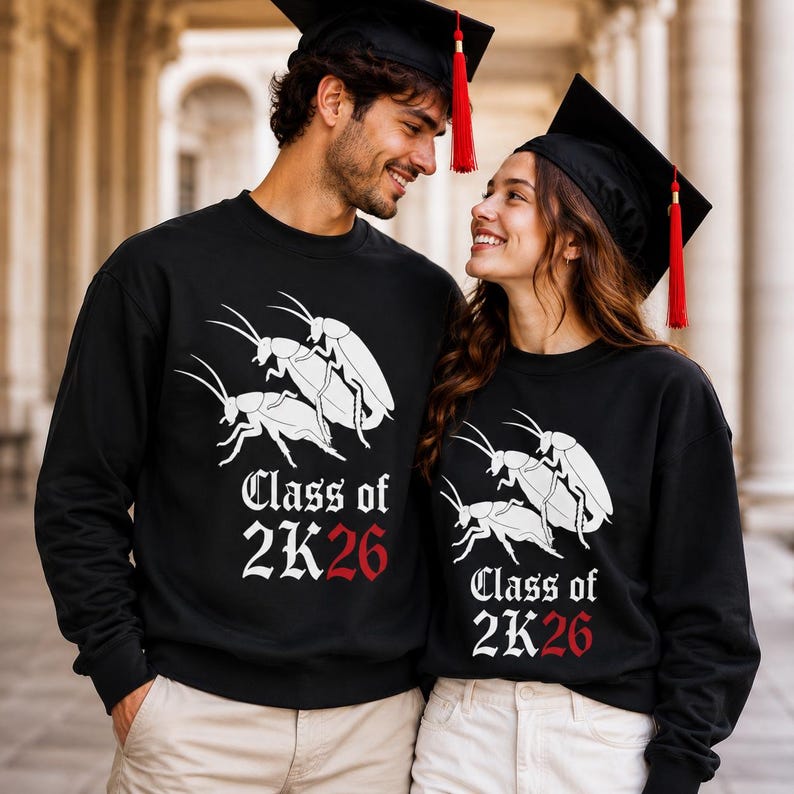 Op de afbeelding: Twee zwarte sweaters met ronde hals voorzien van een witte afbeelding van twee kakkerlakken en de tekst Class of 2K26 in witte en rode letters. Beide kledingstukken worden gedragen met zwarte afstudeerhoeden met rode kwastjes als set.