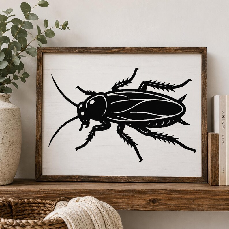 Op de afbeelding: Een rechthoekig wandkunstwerk met een contrastrijk zwart silhouet van een kakkerlak in het midden op een witte achtergrond. Het kunstwerk is gevat in een donkerbruine houten lijst en toont een strak, grafisch ontwerp met scherpe lijnen.