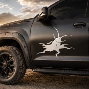 Op de afbeelding: Een matzwarte pick-up truck met een grote witte vinyl sticker op het bestuurdersportier. Het ontwerp toont een gestileerd insect dat uit een grillig, gebarsten oppervlak tevoorschijn komt, geplaatst boven de zwarte treeplank en wielkast.